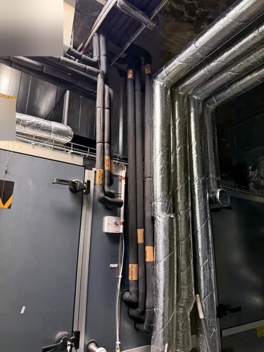 Isolerade rör och ventilationskanaler i ett teknikrum.